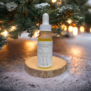 Under Eye and Facial Serum on wooden platform under Christmas tree with festive lights in the background.