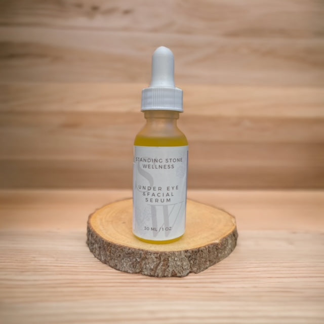 Under Eye and Facial Serum on wooden platform under Christmas tree with festive lights in the background.